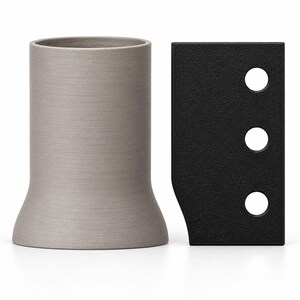 May include: A cylindrical, light gray object with a flared base sits next to a rectangular, black component featuring a textured surface and three circular holes arranged in a vertical line along its right side.