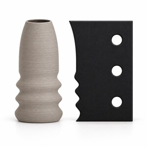 May include: A light gray, textured, cylindrical object with a tapered top and three horizontal ridges at the base, positioned next to a flat, rectangular black tool featuring a curved, serrated edge and three circular holes in a vertical row.