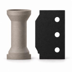 May include: A light gray, cylindrical spool with flared ends and a flat base, positioned next to a rectangular black plate featuring three circular holes aligned vertically along its right side. Both objects are solid and have a matte finish.