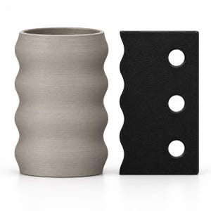 May include: A light gray cylindrical vessel with a wavy, ribbed exterior surface positioned next to a flat, rectangular black object featuring a scalloped edge on one side and three circular cutouts arranged in a vertical line.