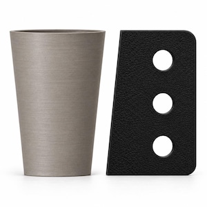 May include: A tapered, smooth-surfaced gray cup positioned next to a black, textured, trapezoidal object featuring three circular cutouts arranged in a vertical line. Both items are set against a plain white background, showcasing their distinct shapes.