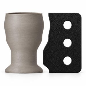 May include: A matte light gray cup with a flared rim and base, positioned next to a rectangular black tool featuring a textured surface and three circular holes arranged in a vertical line along its right side.
