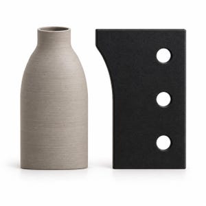 May include: A light grey, cylindrical vase with a textured surface and a narrow neck, positioned next to a rectangular black object featuring a curved side edge and three circular cutouts arranged in a vertical line on its flat surface.