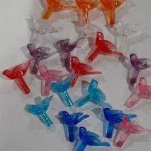 May include: Assortment of colorful bird-shaped Christmas tree ornaments. The ornaments are made of clear plastic and come in shades of orange, pink, blue, and purple.