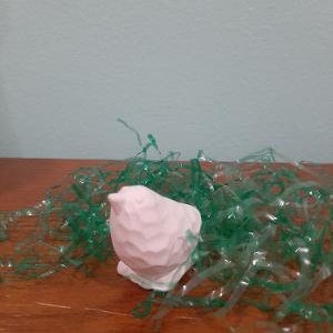 May include: A small, white ceramic bird figurine sitting in a bed of green plastic grass.