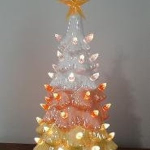 May include: A ceramic Christmas tree with a star topper. The tree is painted in layers of white, orange, and yellow, with small, lit bulbs. The tree is on a wooden surface.