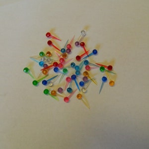 May include: A large assortment of colorful plastic pins with clear plastic stems. The pins are in various colors, including red, blue, green, yellow, and purple.
