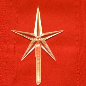 May include: A clear plastic star-shaped Christmas tree topper with a red and white striped stem.