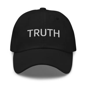 Può includere: Un cappellino da baseball nero con la parola TRUTH ricamata in lettere maiuscole bianche sul pannello frontale. Il cappellino presenta una corona strutturata, una visiera curva e un bottone sulla parte superiore, dal design pulito.