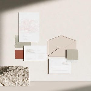 Coordinated wedding invitation stationery with cream cards, muted green accents and an envelope, arranged on a pale background. Fine architectural illustration and small printed text appear on the cards. Digital concept mockup.
