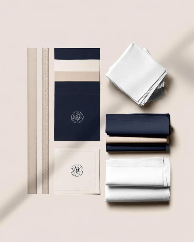 Square navy and cream cocktail napkins with small contrasting monogram letters, displayed with coordinating paper pieces. Digital concept mockup showing a personalised wedding or event table detail.