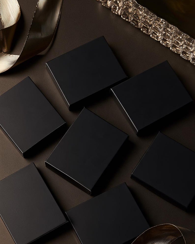 Dark matchbox mockups styled for an evening celebration, with plain and gold-toned decorative sleeve designs. The presentation shows compact rectangular boxes for personalised party favours.