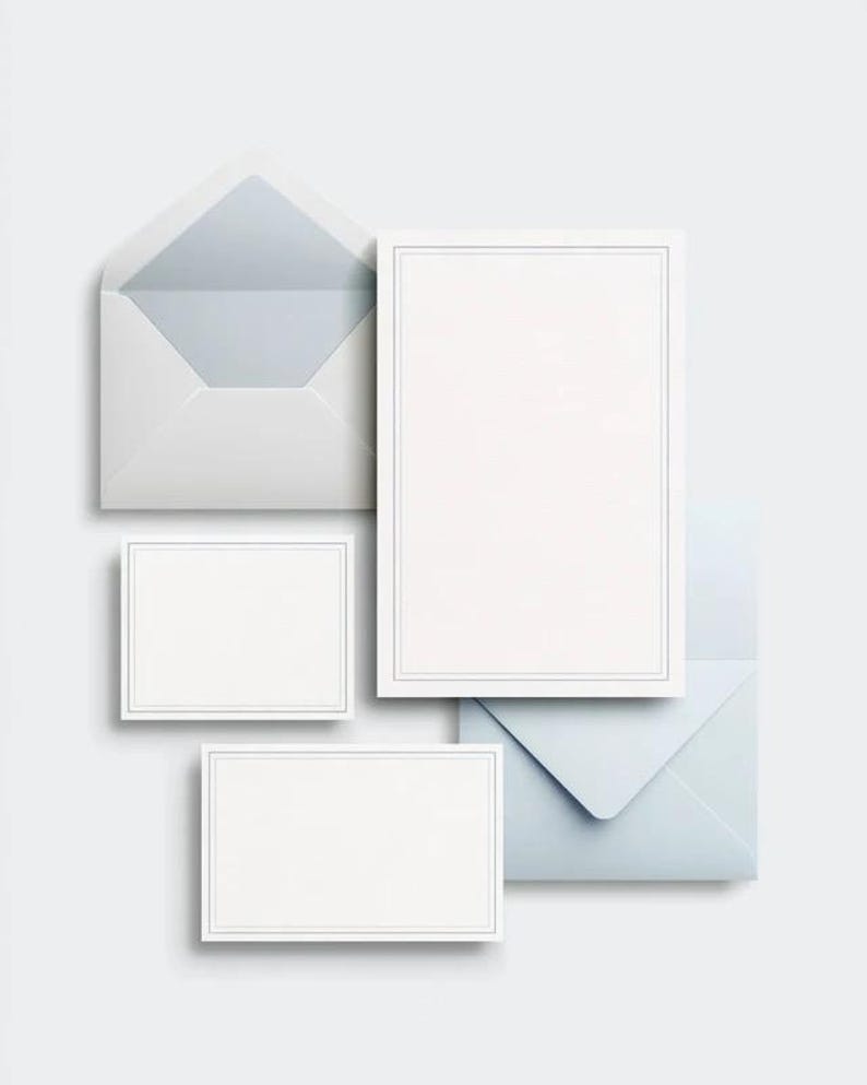 Unprinted cream invitation cards in several rectangular sizes with matching envelopes, arranged on a pale background. The mockup shows a coordinated wedding invitation, reply card and details-card format.