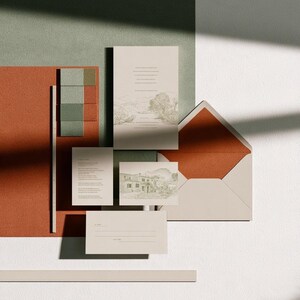 Coordinated wedding invitation stationery with cream cards, muted green accents and an envelope, arranged on a pale background. Fine architectural illustration and small printed text appear on the cards. Digital concept mockup.