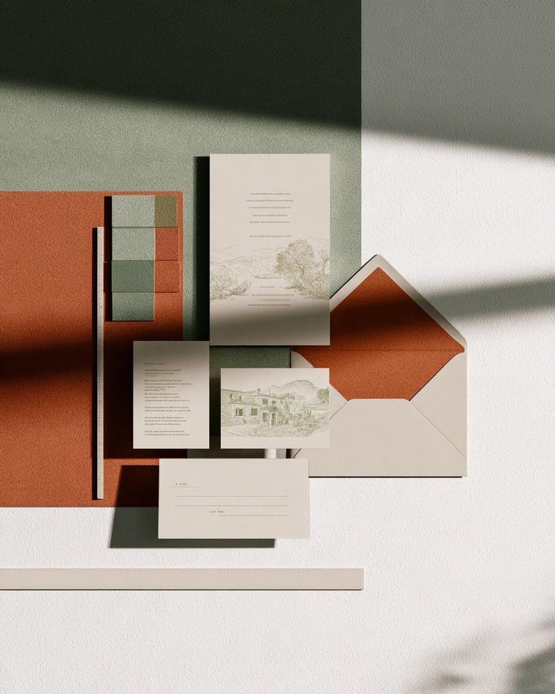Coordinated wedding invitation stationery with cream cards, muted green accents and an envelope, arranged on a pale background. Fine architectural illustration and small printed text appear on the cards. Digital concept mockup.