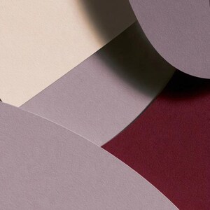 Layered unprinted menu-card mockups with curved paper edges in cream and muted burgundy tones. The arrangement shows contrasting paper shapes and soft shadows for a modern table-stationery design.