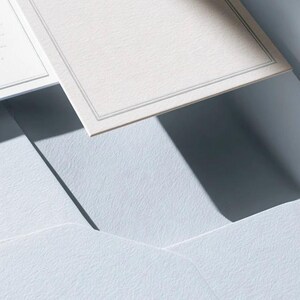 Unprinted cream invitation cards in several rectangular sizes with matching envelopes, arranged on a pale background. The mockup shows a coordinated wedding invitation, reply card and details-card format.