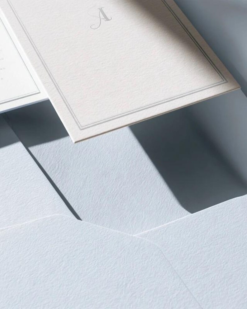 Unprinted cream invitation cards in several rectangular sizes with matching envelopes, arranged on a pale background. The mockup shows a coordinated wedding invitation, reply card and details-card format.