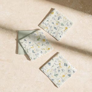 Square cocktail-napkin and paper-detail mockups with fine botanical line illustrations, styled with coordinating paper pieces. Digital presentation of a custom illustrated wedding and event design.