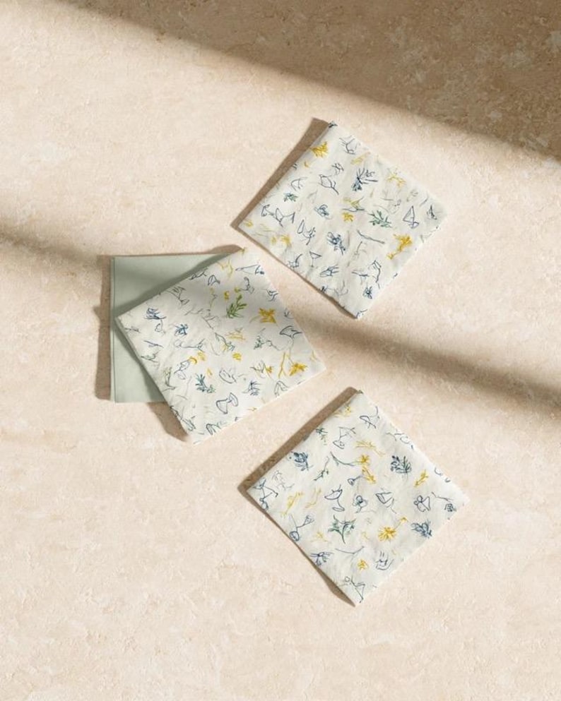 Square cocktail-napkin and paper-detail mockups with fine botanical line illustrations, styled with coordinating paper pieces. Digital presentation of a custom illustrated wedding and event design.