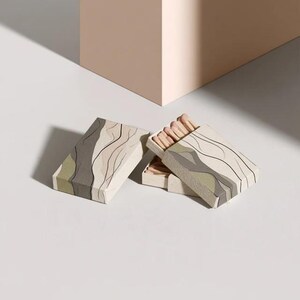 Cream rectangular drawer-style matchbox mockups arranged with coordinating neutral paper samples. The presentation shows sleeves, trays and the compact box proportions for bespoke event designs.