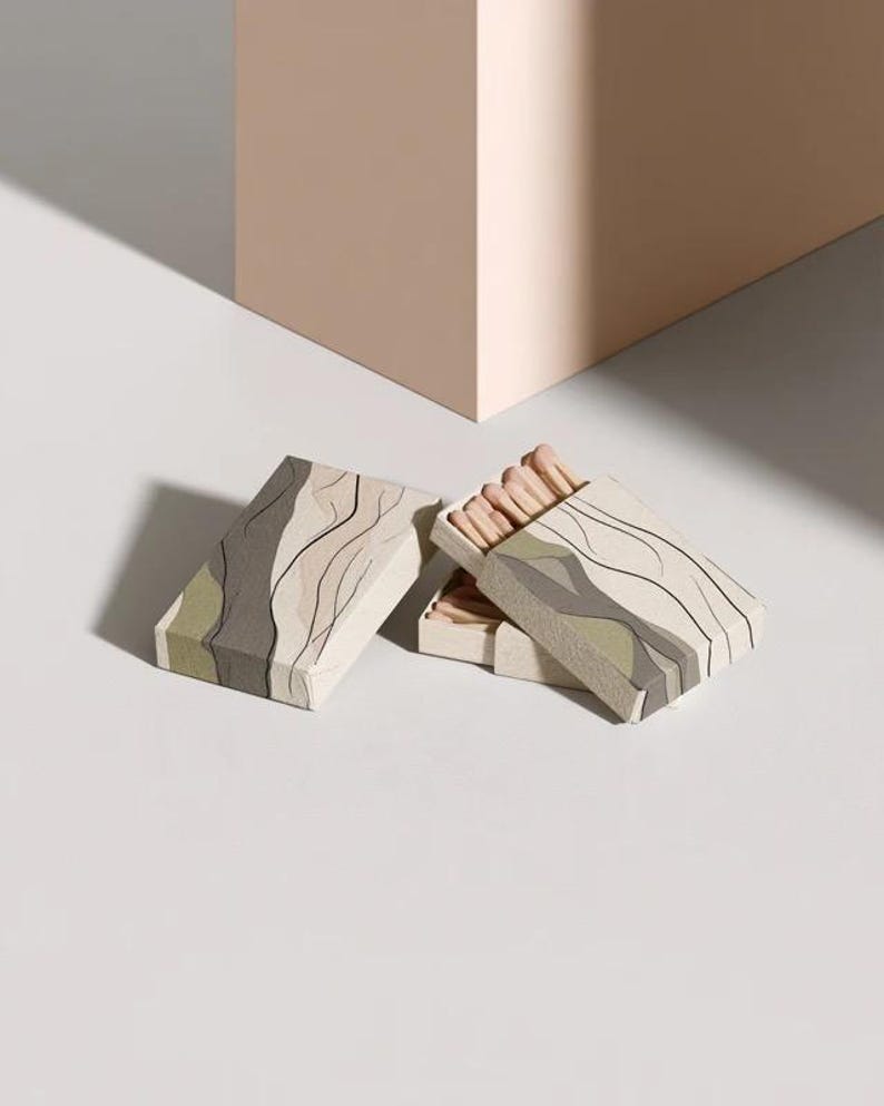 Cream rectangular drawer-style matchbox mockups arranged with coordinating neutral paper samples. The presentation shows sleeves, trays and the compact box proportions for bespoke event designs.