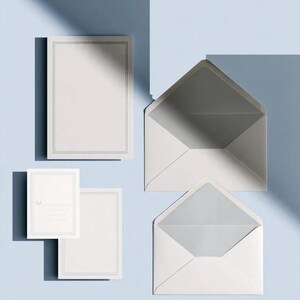 Unprinted cream invitation cards in several rectangular sizes with matching envelopes, arranged on a pale background. The mockup shows a coordinated wedding invitation, reply card and details-card format.