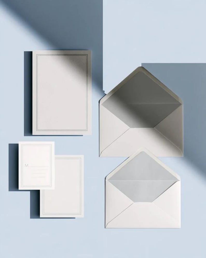 Unprinted cream invitation cards in several rectangular sizes with matching envelopes, arranged on a pale background. The mockup shows a coordinated wedding invitation, reply card and details-card format.