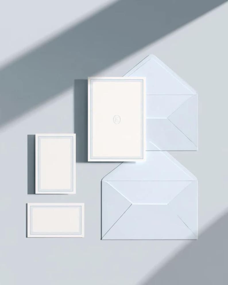 Unprinted cream invitation cards in several rectangular sizes with matching envelopes, arranged on a pale background. The mockup shows a coordinated wedding invitation, reply card and details-card format.
