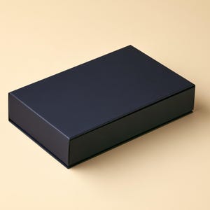 AI-assisted studio design visual of a closed navy drawer-style matchbox on an ivory background. Illustrates the broad 14.5 x 10.5 x 3.5 cm outside box format; final artwork and colours are agreed in your proof.