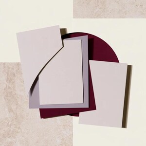 Layered unprinted menu-card mockups with curved paper edges in cream and muted burgundy tones. The arrangement shows contrasting paper shapes and soft shadows for a modern table-stationery design.