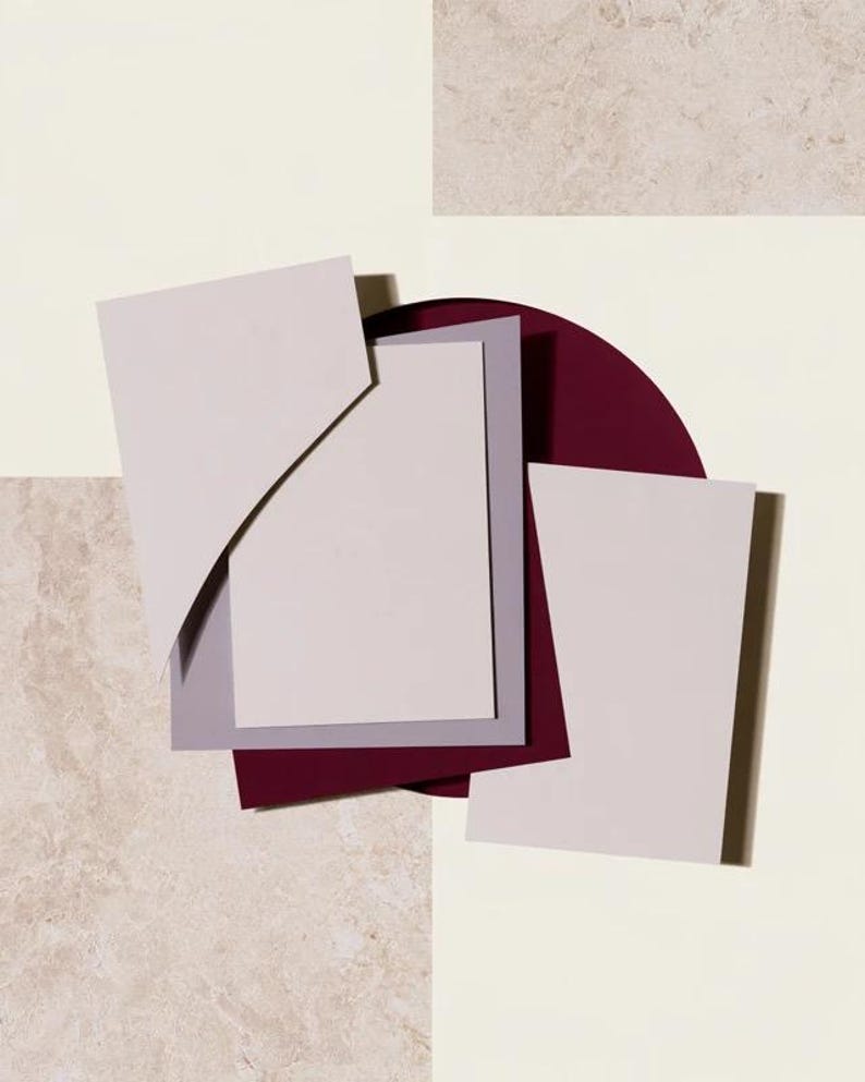 Layered unprinted menu-card mockups with curved paper edges in cream and muted burgundy tones. The arrangement shows contrasting paper shapes and soft shadows for a modern table-stationery design.