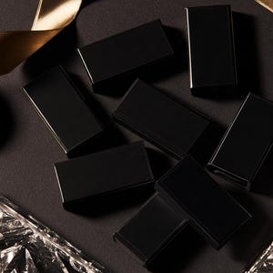 Dark matchbox mockups styled for an evening celebration, with plain and gold-toned decorative sleeve designs. The presentation shows compact rectangular boxes for personalised party favours.