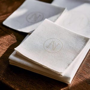 Square navy and cream cocktail napkins with small contrasting monogram letters, displayed with coordinating paper pieces. Digital concept mockup showing a personalised wedding or event table detail.