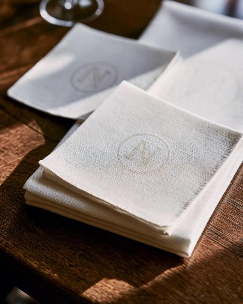 Square navy and cream cocktail napkins with small contrasting monogram letters, displayed with coordinating paper pieces. Digital concept mockup showing a personalised wedding or event table detail.