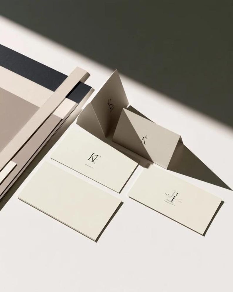 Cream wedding place cards with small dark initials and fine lettering, shown as flat and folded cards on a pale surface. Digital concept mockup of personalised table stationery.