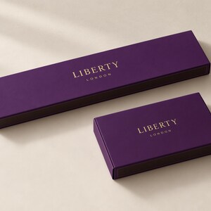 Concept mockup of purple matchboxes in 28cm and 14.5cm formats, featuring gold Liberty London lettering.