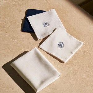 Square navy and cream cocktail napkins with small contrasting monogram letters, displayed with coordinating paper pieces. Digital concept mockup showing a personalised wedding or event table detail.