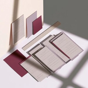 Layered unprinted menu-card mockups with curved paper edges in cream and muted burgundy tones. The arrangement shows contrasting paper shapes and soft shadows for a modern table-stationery design.