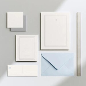 Unprinted cream invitation cards in several rectangular sizes with matching envelopes, arranged on a pale background. The mockup shows a coordinated wedding invitation, reply card and details-card format.