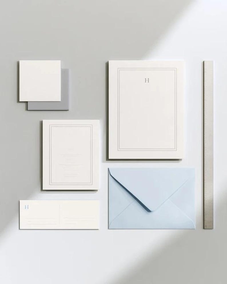 Unprinted cream invitation cards in several rectangular sizes with matching envelopes, arranged on a pale background. The mockup shows a coordinated wedding invitation, reply card and details-card format.