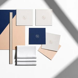 Square navy and cream cocktail napkins with small contrasting monogram letters, displayed with coordinating paper pieces. Digital concept mockup showing a personalised wedding or event table detail.