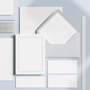 Unprinted cream invitation cards in several rectangular sizes with matching envelopes, arranged on a pale background. The mockup shows a coordinated wedding invitation, reply card and details-card format.