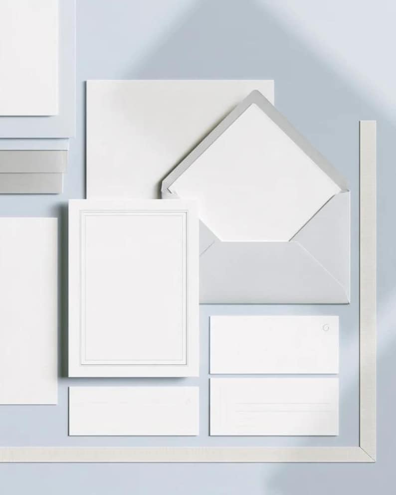 Unprinted cream invitation cards in several rectangular sizes with matching envelopes, arranged on a pale background. The mockup shows a coordinated wedding invitation, reply card and details-card format.