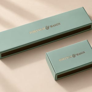 Concept mockup of blue-green matchboxes in 28cm and 14.5cm formats, featuring gold Fortnum & Mason lettering.