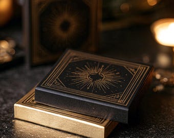 May include: Two rectangular boxes stacked on each other. The top box is black with gold foil sunburst illustrations and geometric border lines. The bottom box is solid gold with black geometric border lines. Both boxes have a matte finish.