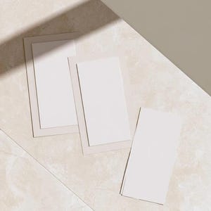Layered unprinted menu-card mockups with curved paper edges in cream and muted burgundy tones. The arrangement shows contrasting paper shapes and soft shadows for a modern table-stationery design.