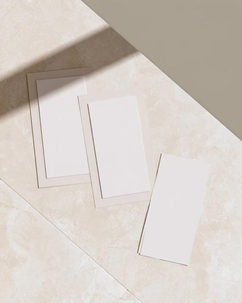 Layered unprinted menu-card mockups with curved paper edges in cream and muted burgundy tones. The arrangement shows contrasting paper shapes and soft shadows for a modern table-stationery design.