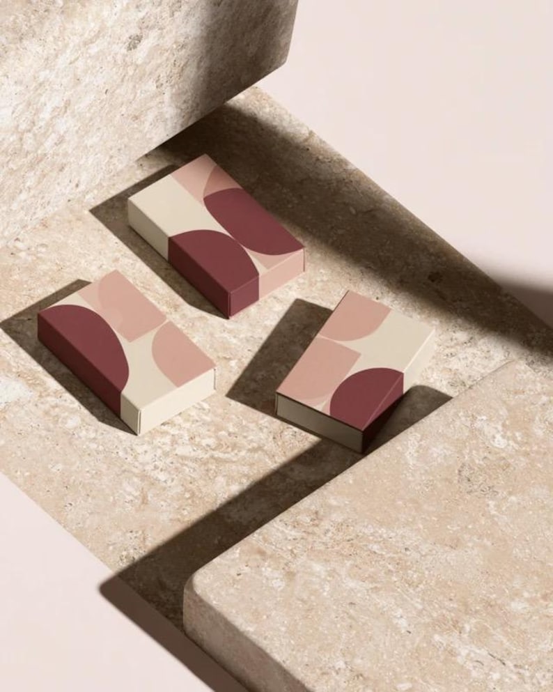Contemporary matchbox mockup with a coloured paper sleeve and a clean graphic layout. The rectangular box is presented in soft directional light as a personalised wedding or event favour concept.