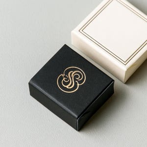 Small rectangular matchbox mockups in a restrained neutral palette, decorated with fine monograms. The styled arrangement shows the paper sleeves and drawer-style construction for personalised event favours.
